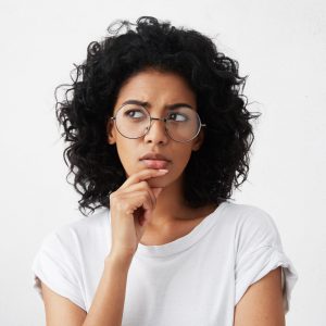 Isolated portrait of stylish young mixed race woman with dark shaggy hair touching her chin and looking sideways with doubtful and sceptical expression, suspecting her boyfriend of lying to her femme qui réfléchit