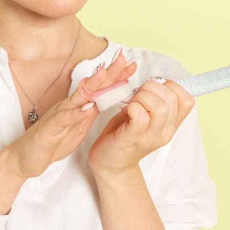 vue-face-jeune-femme-seduisante-chemise-blanche-fixant-ses-ongles-surface-vert-clair se faire une manucure